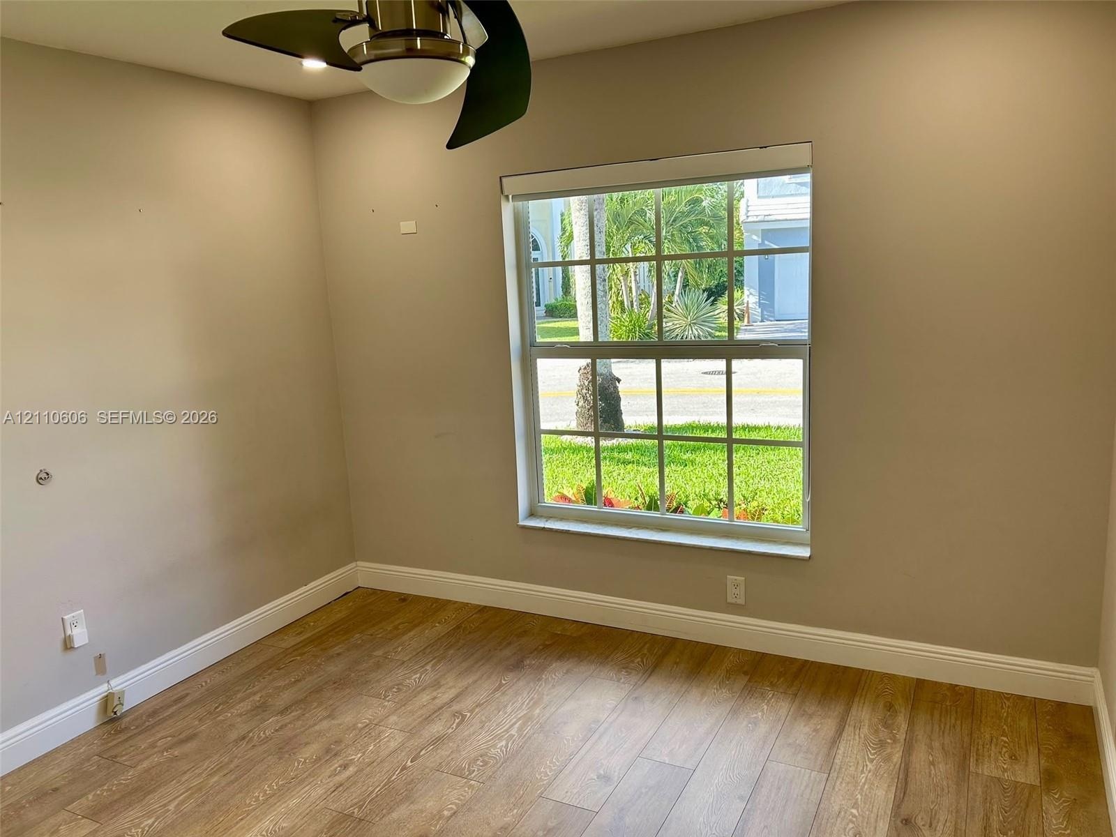 Neutral interior space featuring wood-finish flooring, a multi-pane window with a muntin grid, and an attached ceiling fan with integrated lighting