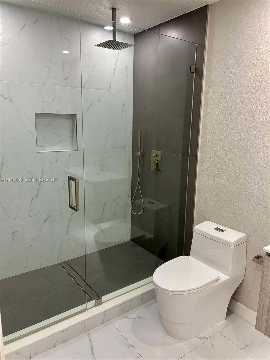 Walk-in shower featuring a frameless glass enclosure, rainfall showerhead, recessed storage niche, and contrast stone-finish tiling, paired with a mod