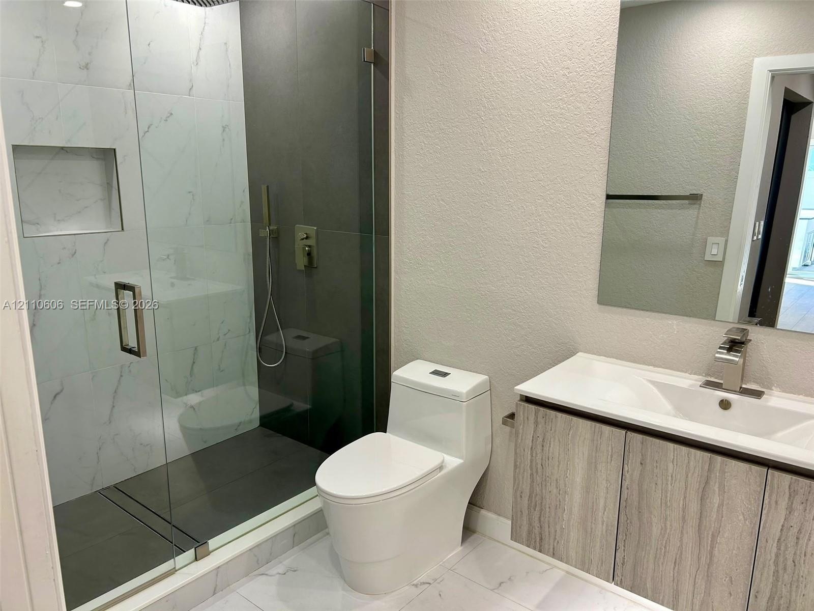 Walk-in shower with floor-to-ceiling tiled walls and a recessed niche, frameless glass enclosure, wood-finish vanity with an integrated countertop sin
