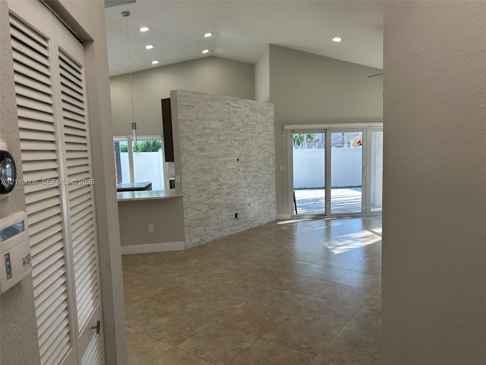 Vaulted ceilings featuring recessed lighting, a stone-finish accent wall, and large-format tile flooring, complemented by sliding glass doors leading 