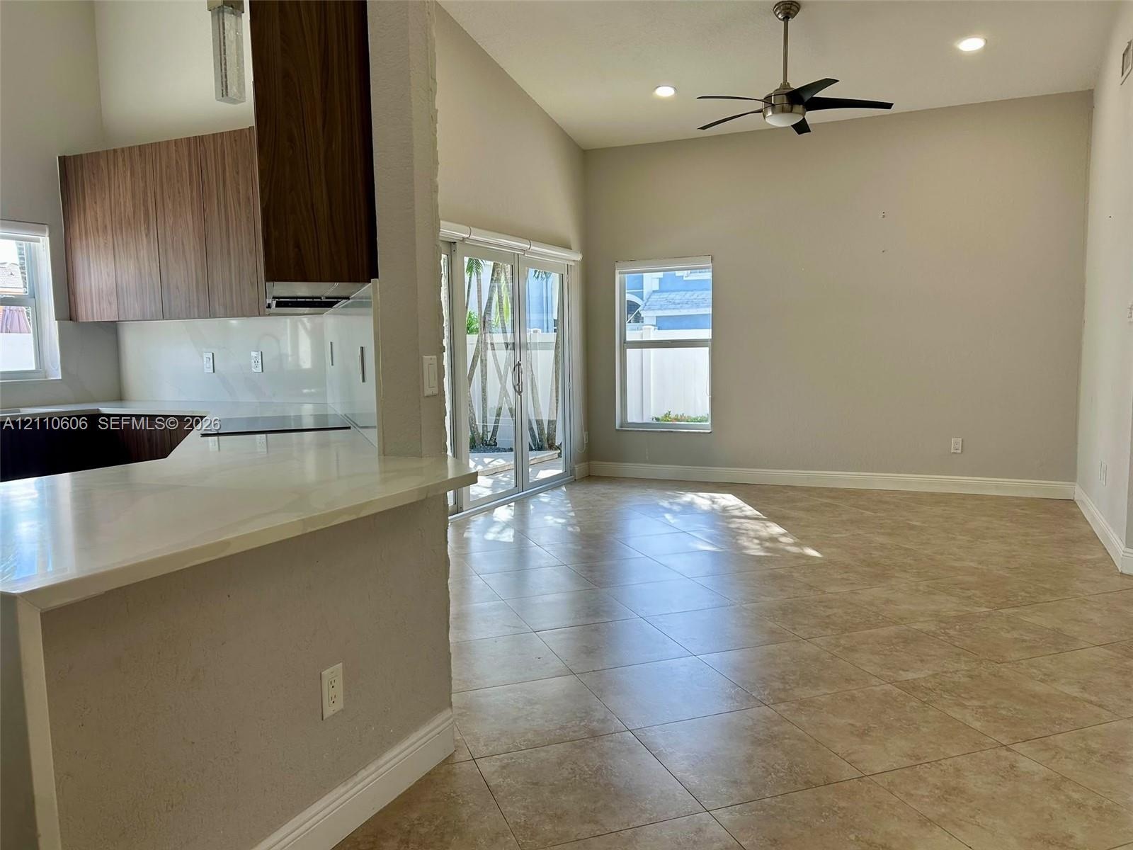 Open-concept interior featuring vaulted ceilings, neutral tile flooring, wood-finish cabinetry, white solid-surface countertops, and sliding glass doo