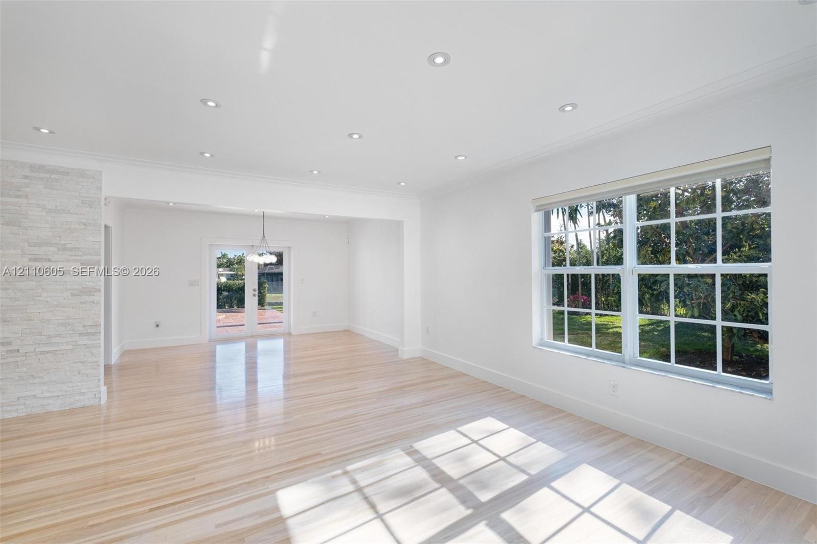 Light-filled interior featuring wood-finish flooring, recessed lighting, a stone-textured accent wall, multi-pane windows, and glass-paned double door