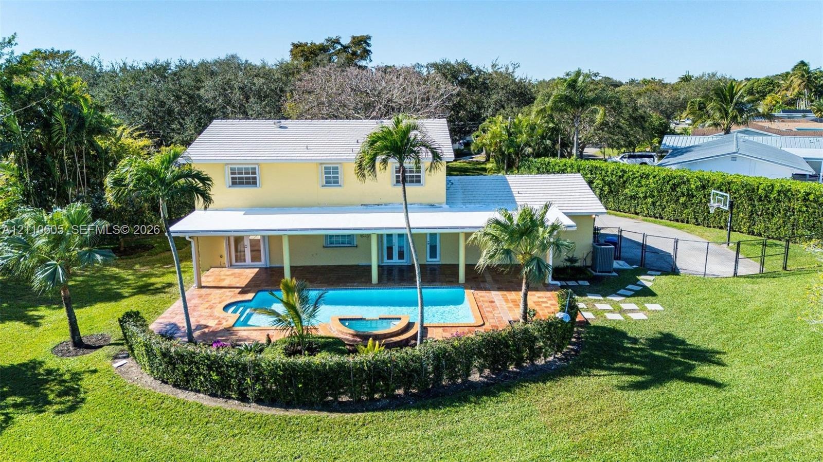Two-story exterior featuring a covered patio, tiled pool deck, in-ground pool with integrated spa, and expansive lawn