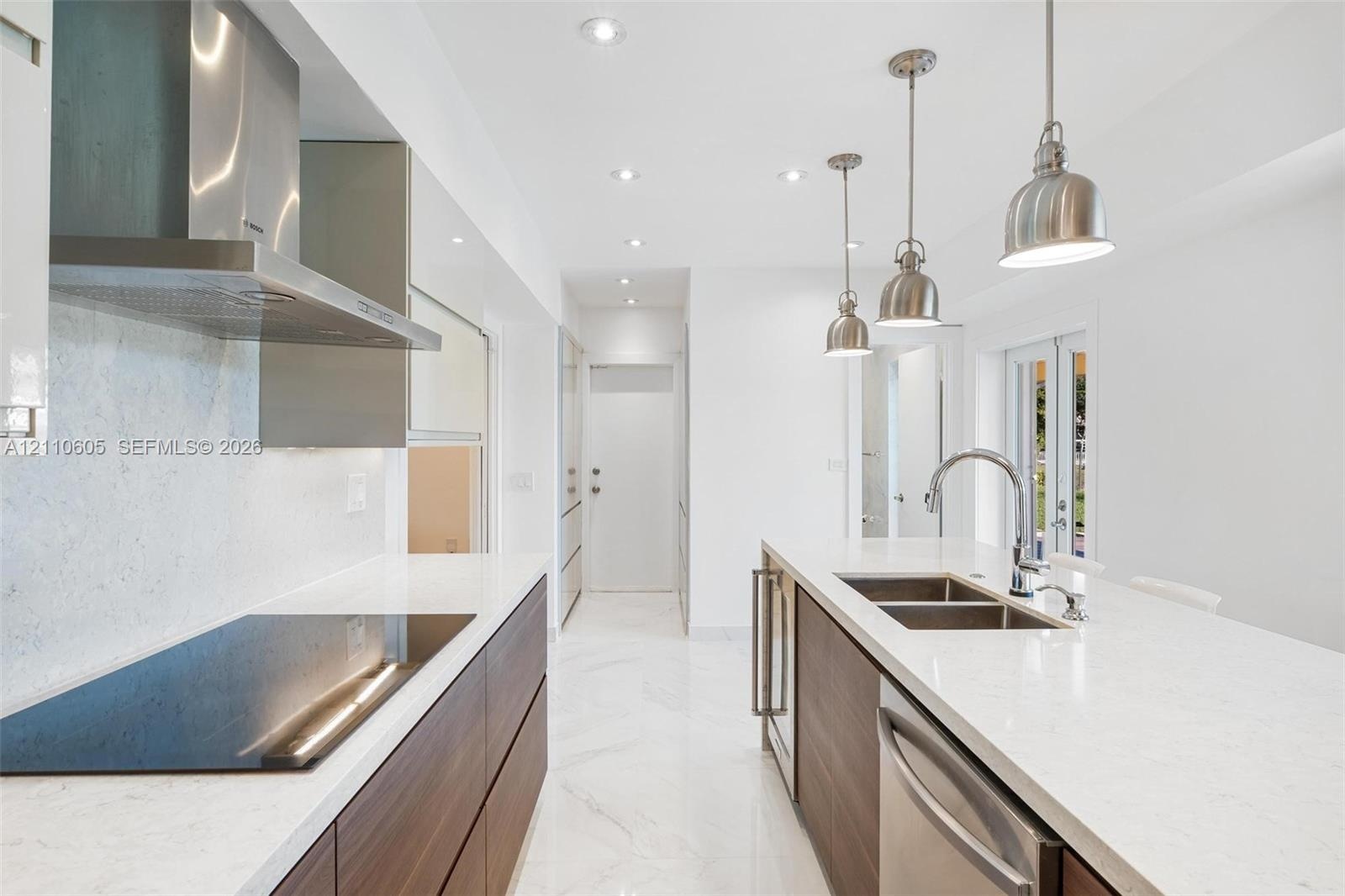 Modern kitchen featuring wood-finish flat-panel cabinetry, light-toned stone-look countertops, stainless steel appliances, marble-patterned flooring, 