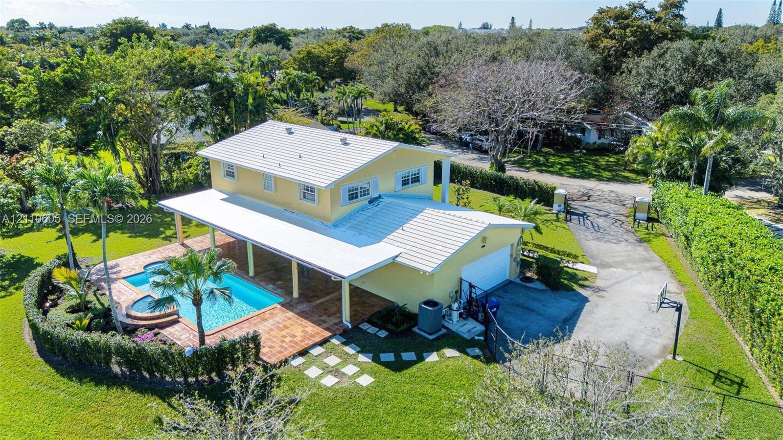 Two-story residence featuring a metal roof, an expansive covered patio, a tiled pool with an integrated spa, and a paved driveway situated on a large,