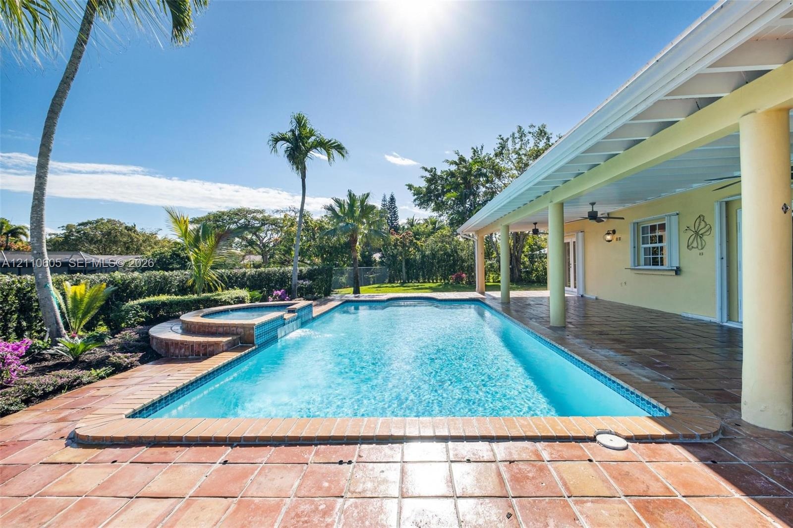 Covered patio featuring a ceramic tile floor and ceiling-mounted fans, overlooking a swimming pool with an integrated raised spa and brick-finished co
