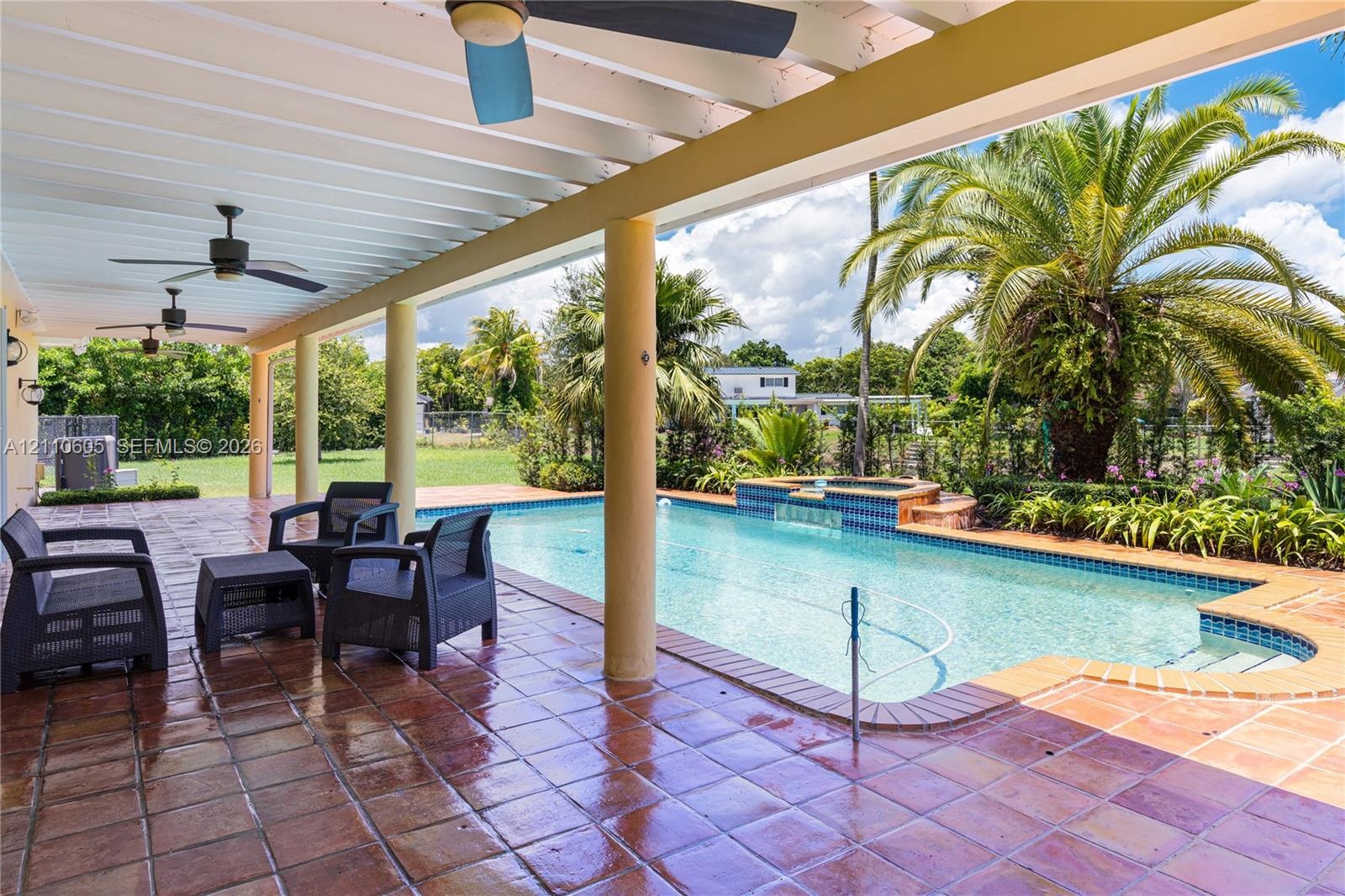 Covered patio with terracotta tile flooring, ceiling fans, in-ground swimming pool, integrated spillover spa, and mature landscaping
