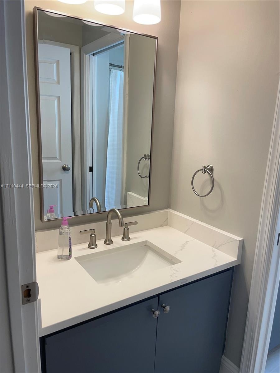 Bathroom vanity featuring a stone-composite countertop with integrated sink, polished chrome widespread faucet, navy blue cabinetry, and a framed rect