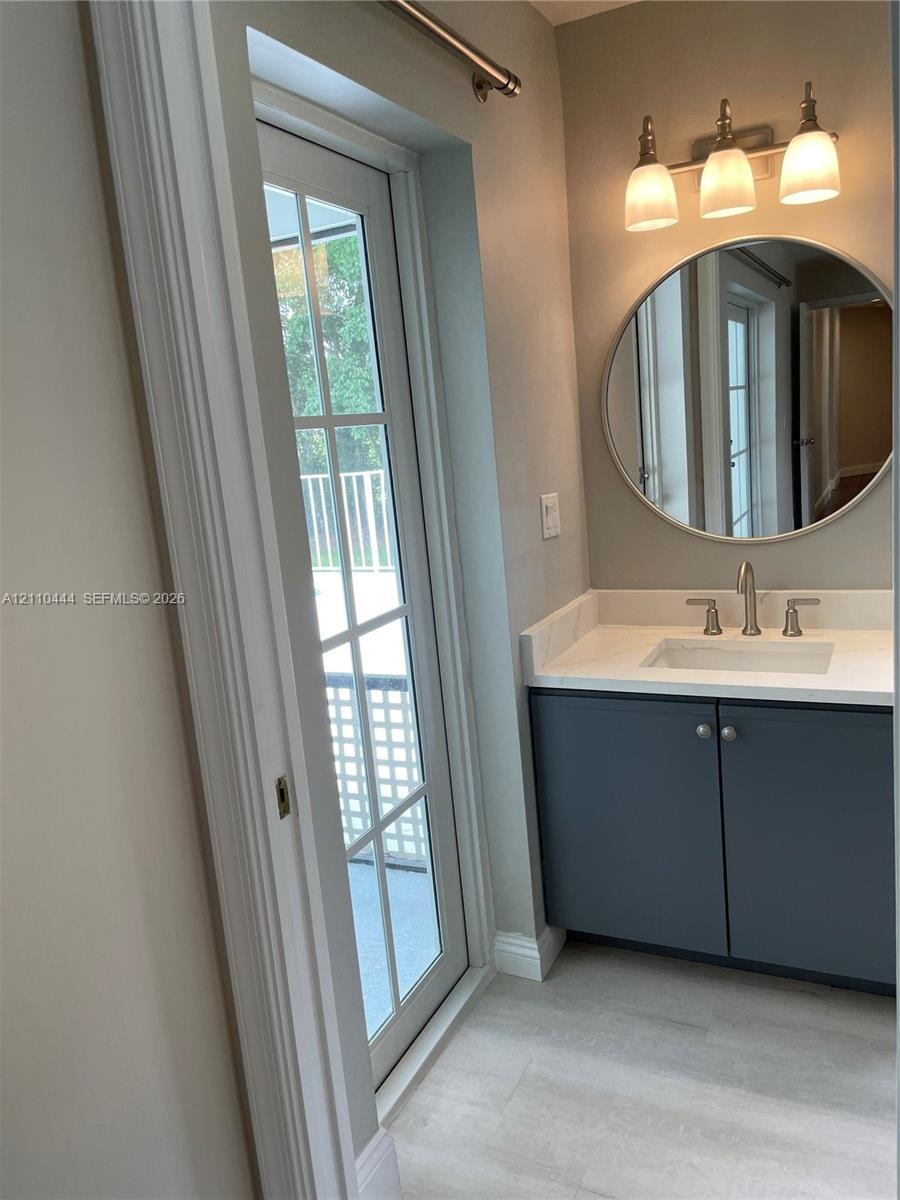 Vanity featuring a solid-surface countertop, integrated rectangular sink, dark cabinetry with hardware, a circular wall-mounted mirror, and a three-li