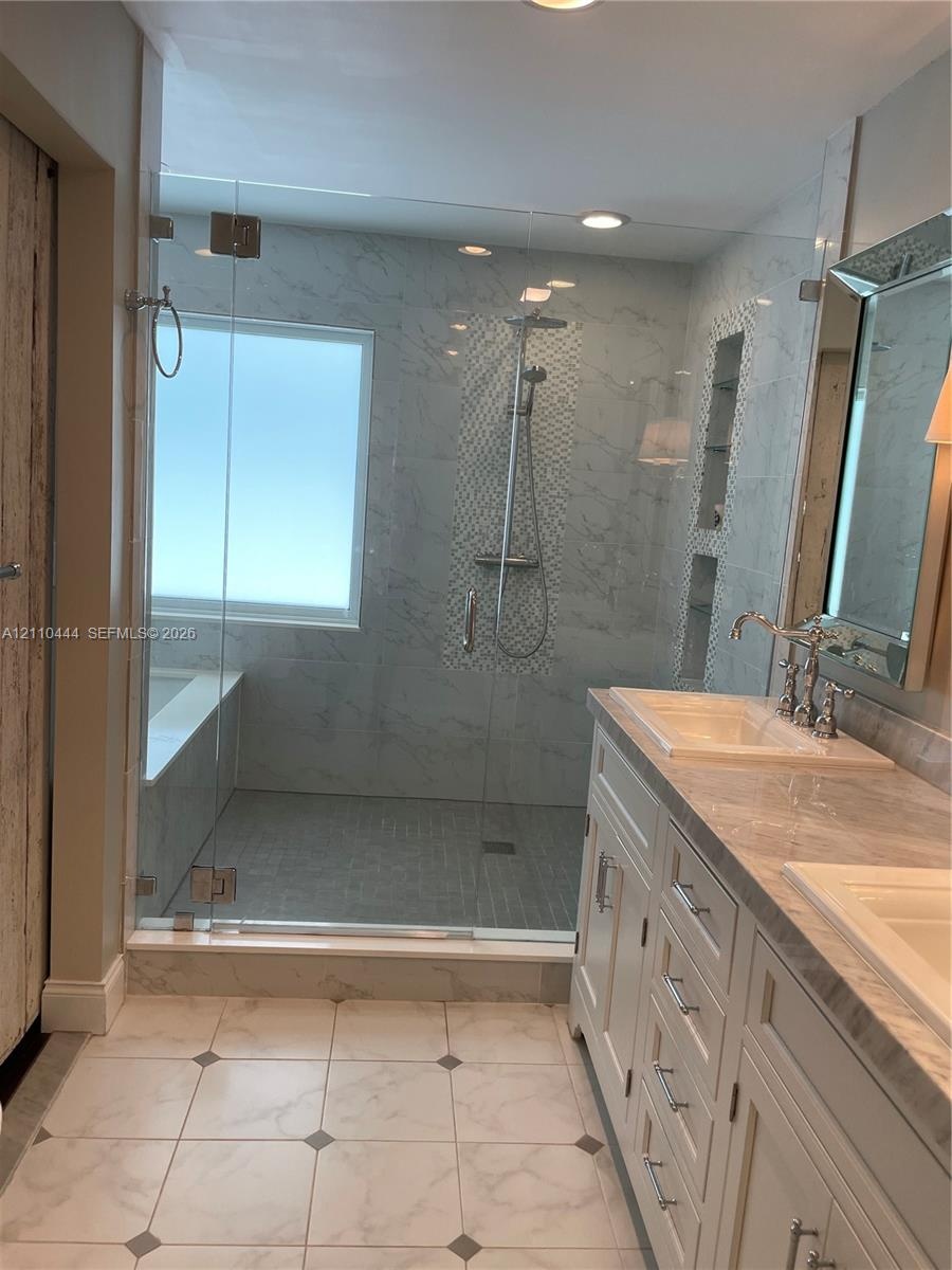 Walk-in shower featuring glass paneling, floor-to-ceiling tile, and built-in shelving, paired with a dual-sink vanity with stone-finish countertops an