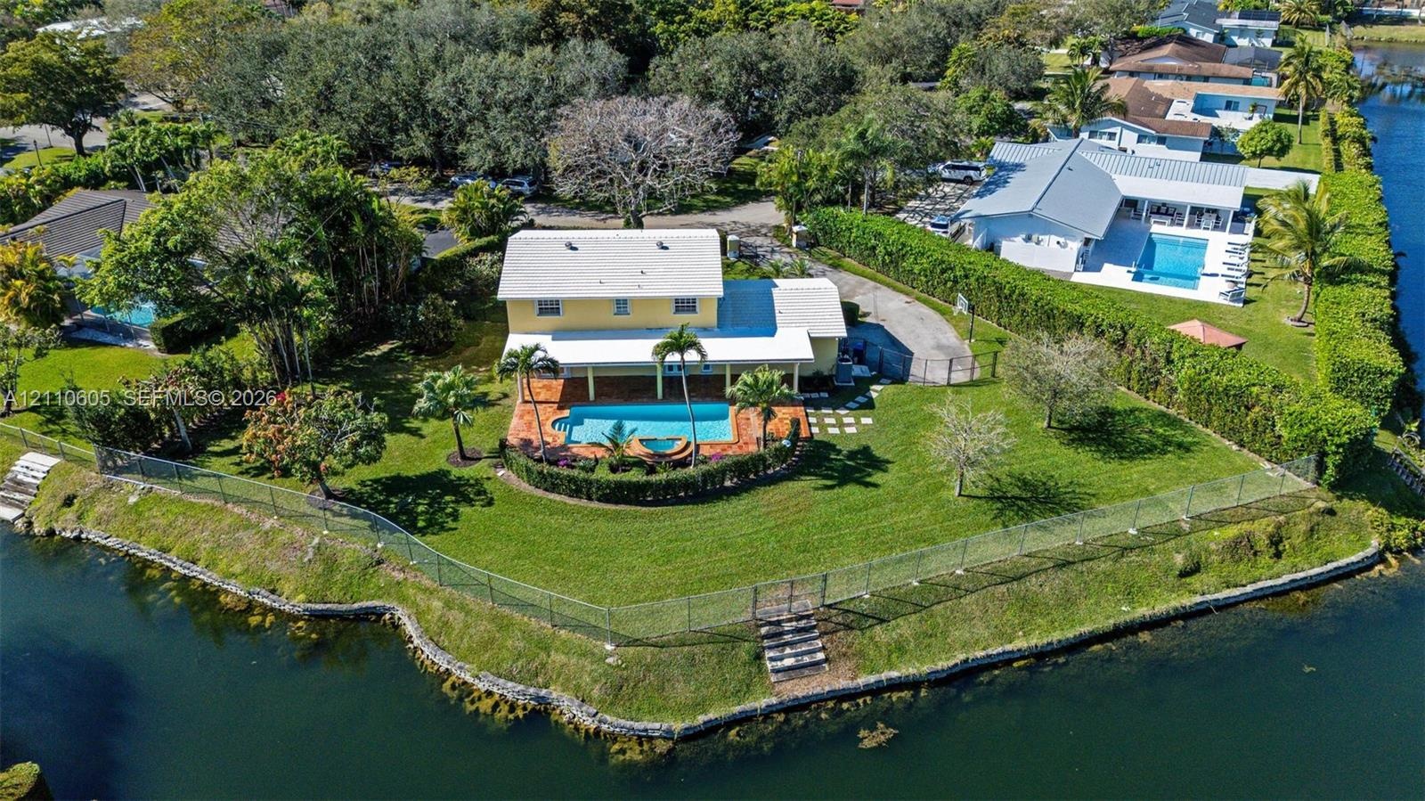 Waterfront property featuring a swimming pool, covered patio, fenced perimeter, and mature landscaping