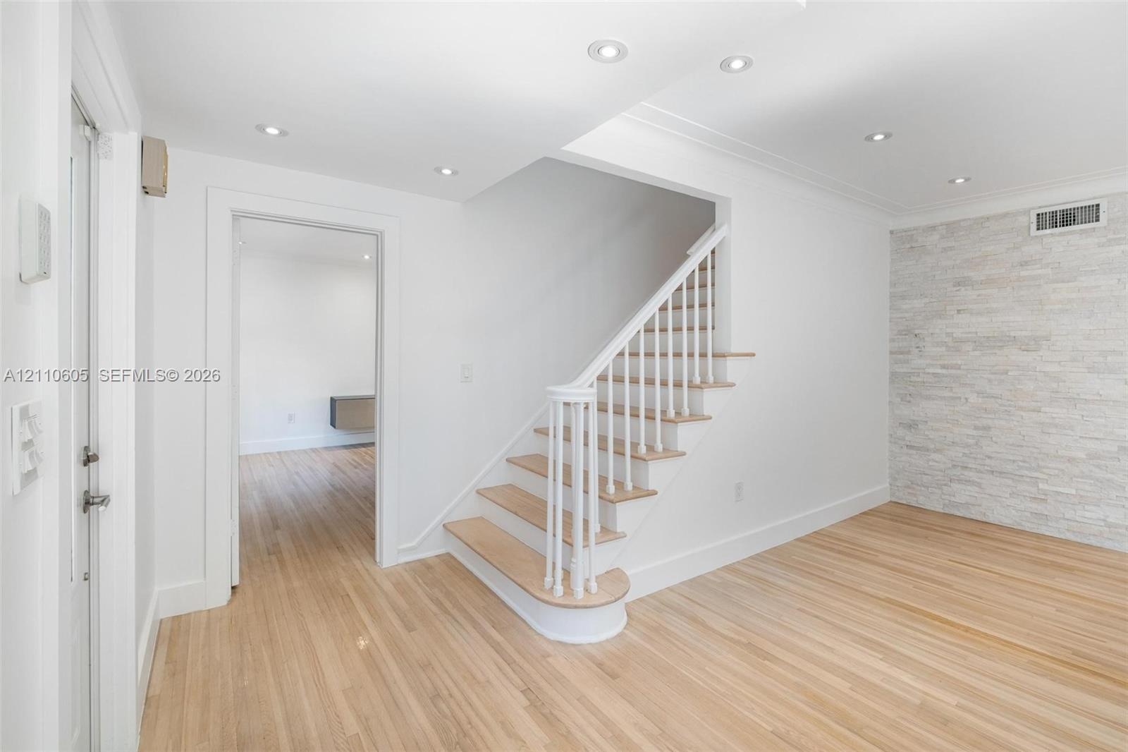 Staircase featuring white balusters and wood-finish treads, natural wood-finish flooring, recessed lighting, and a floor-to-ceiling stacked stone acce