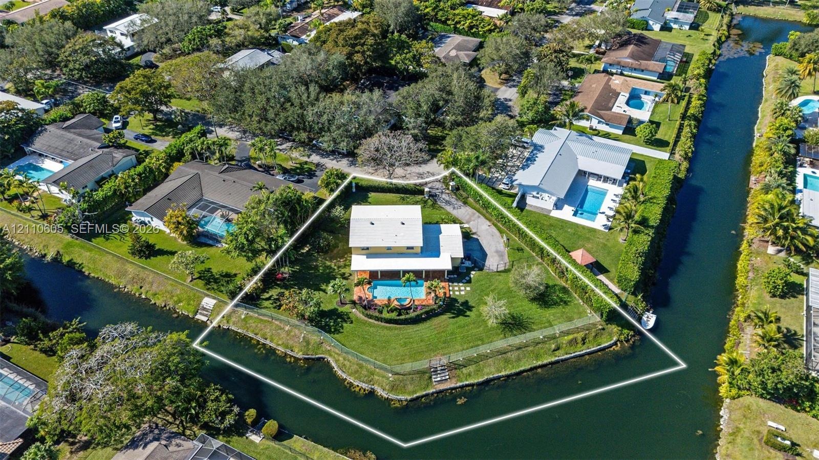 Aerial view of a waterfront property featuring a canal-front lot, a private swimming pool, a sprawling lawn, and mature perimeter landscaping