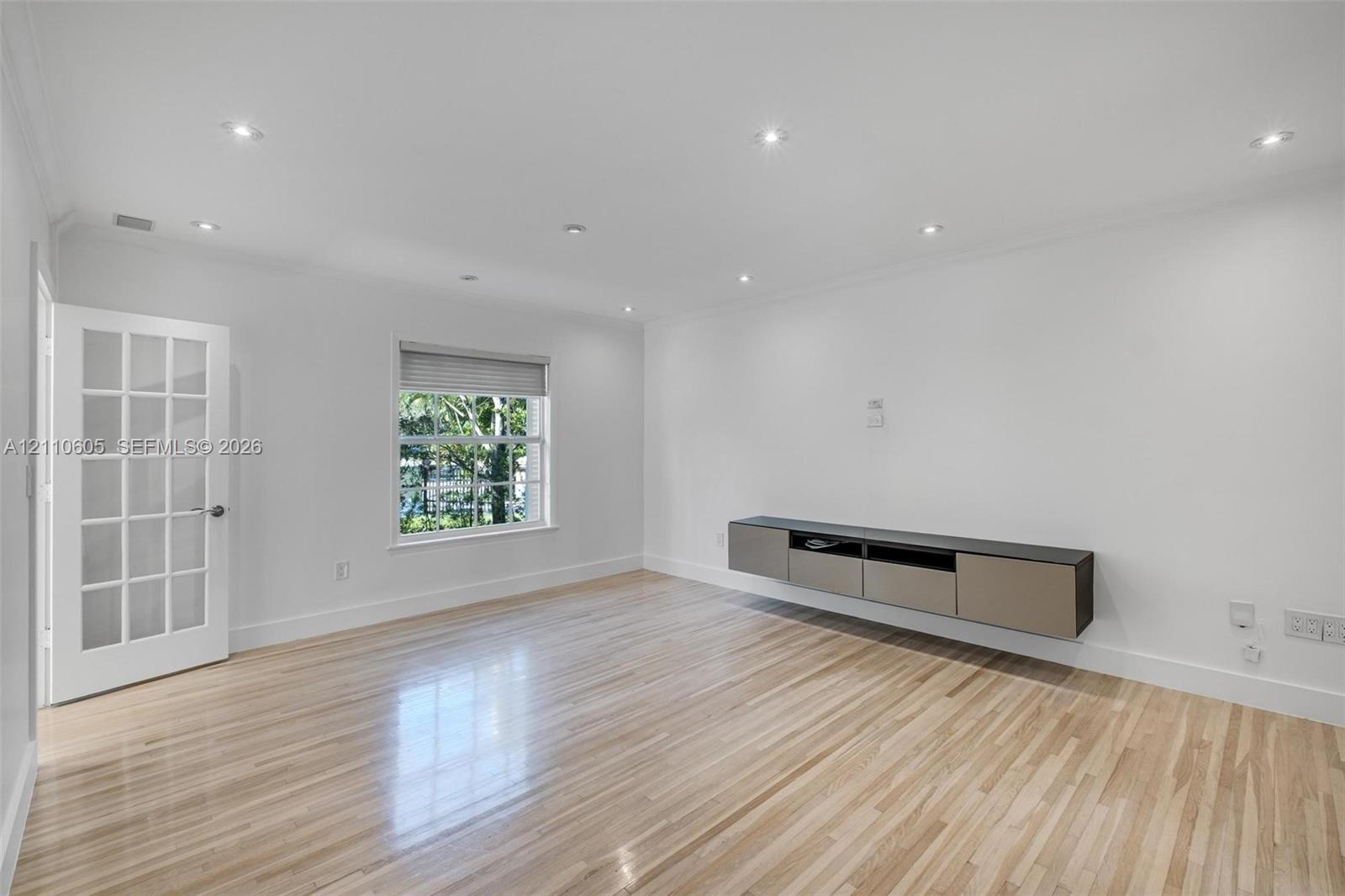 Light-filled room featuring wood-finish flooring, a floating wall-mounted cabinet, recessed lighting, and a multi-pane glass-panel door