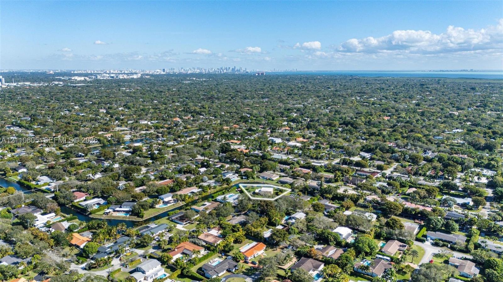 Aerial perspective of a residential lot featuring mature tree canopy, canal frontage, and suburban greenery