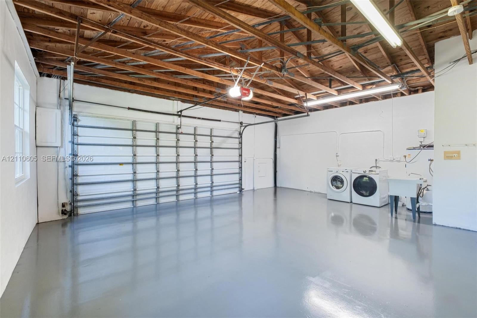 Multi-vehicle garage featuring an exposed wood-beam ceiling, finished epoxy flooring, a sectional roll-up door, and a built-in utility sink
