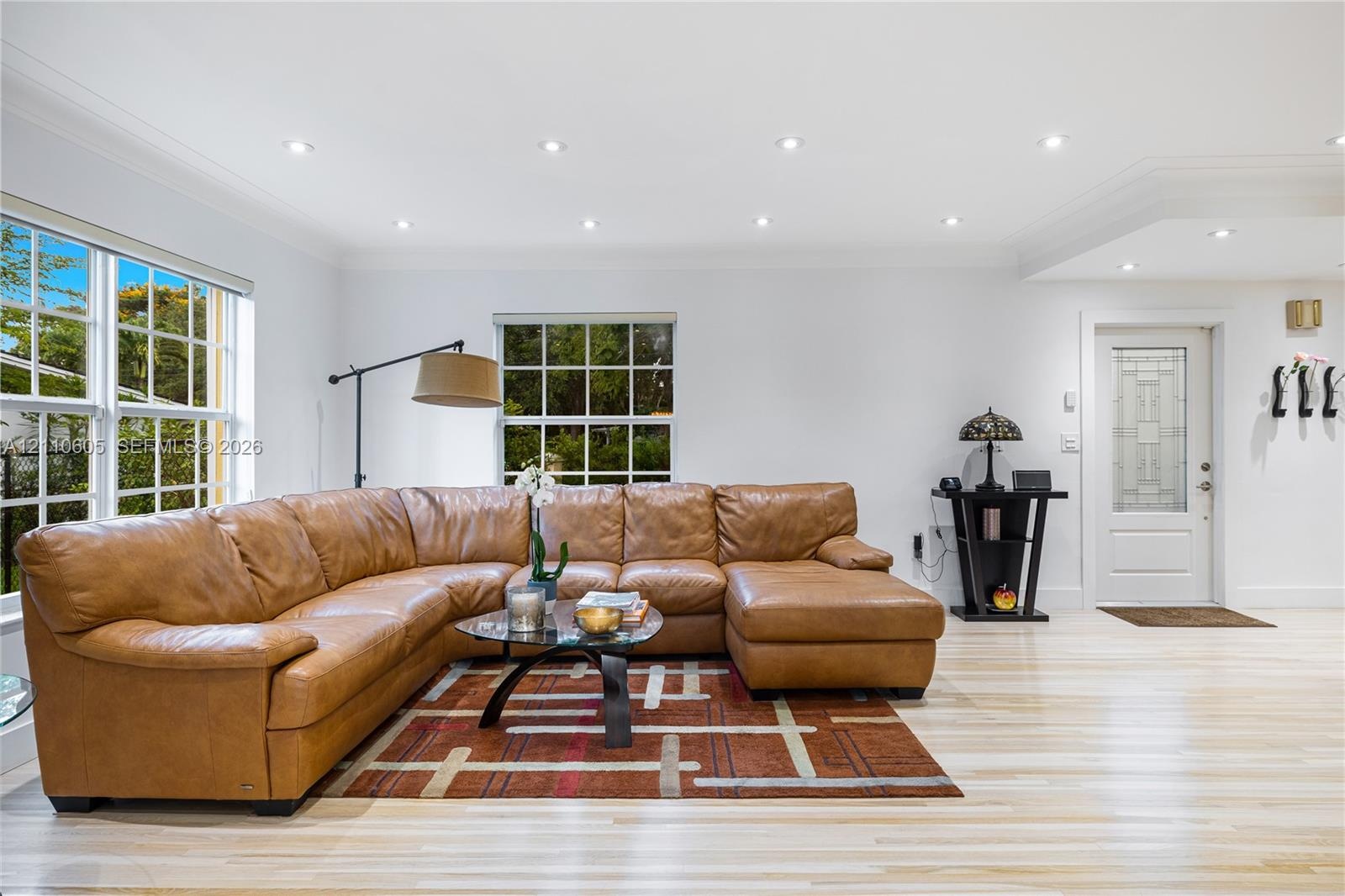 Living area featuring light-toned wood-finish flooring, recessed lighting, multi-pane windows, and a glass-paneled entry door