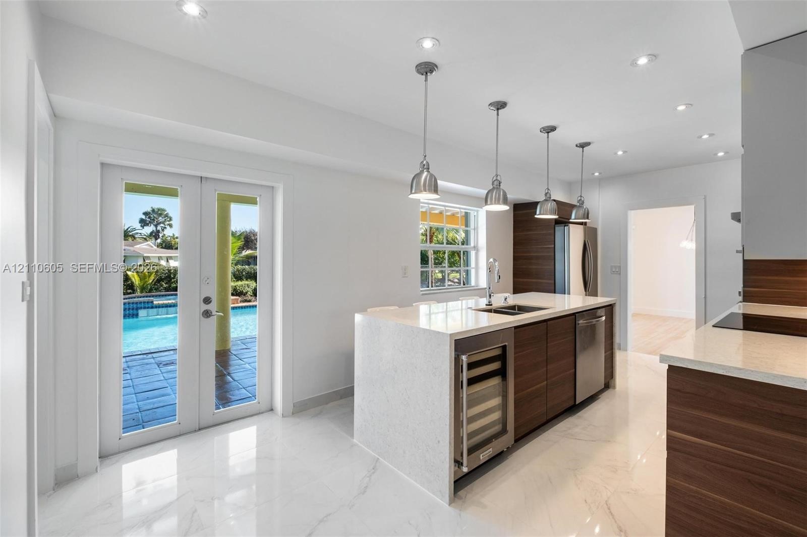 Kitchen featuring a waterfall-edge quartz island, wood-finish cabinetry, recessed lighting, stone-finish flooring, and glass-paneled double doors