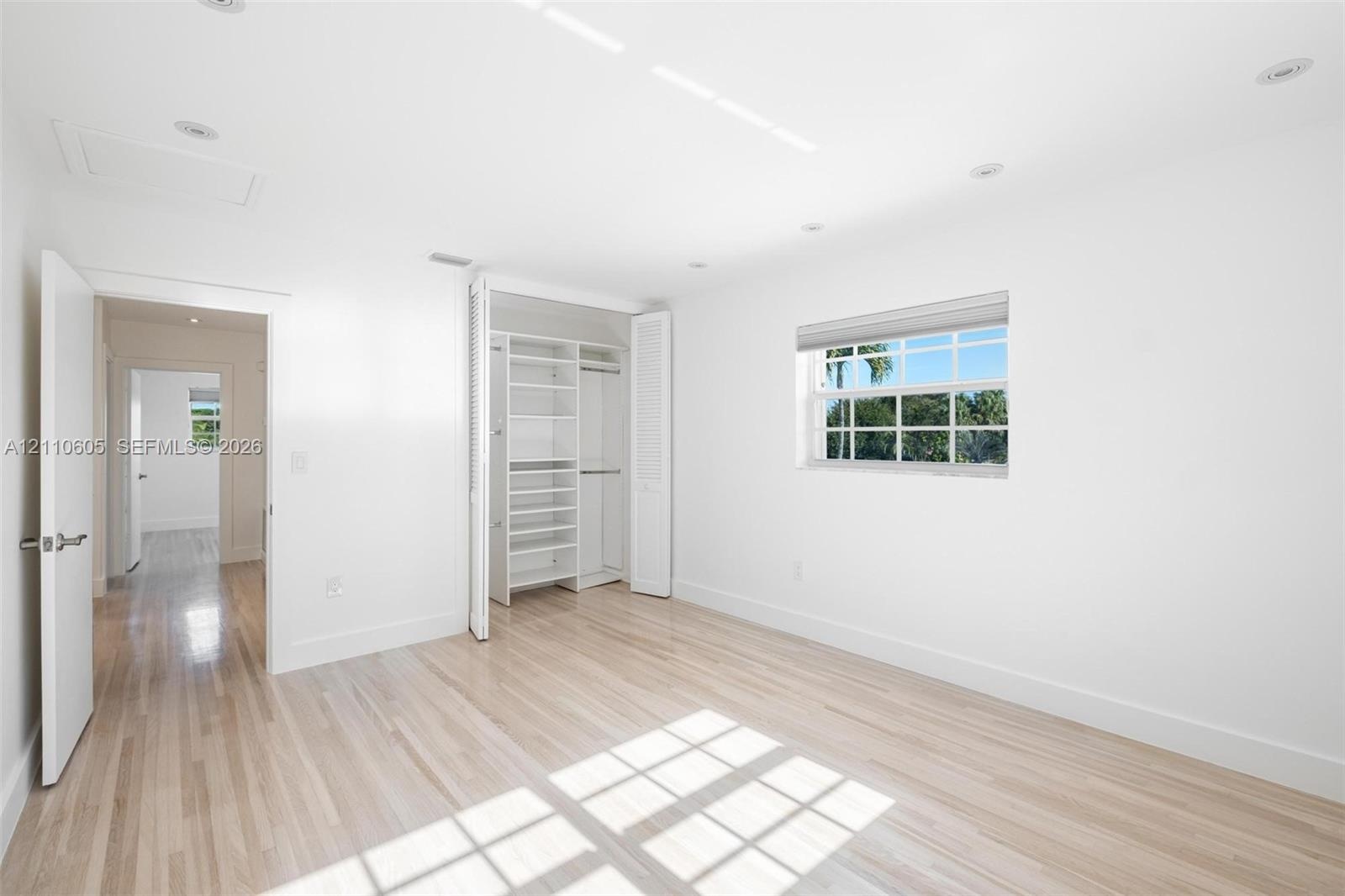 Room featuring light-toned wood-finish flooring, recessed lighting, a single-hung window, and a built-in closet system with open shelving and hanging 