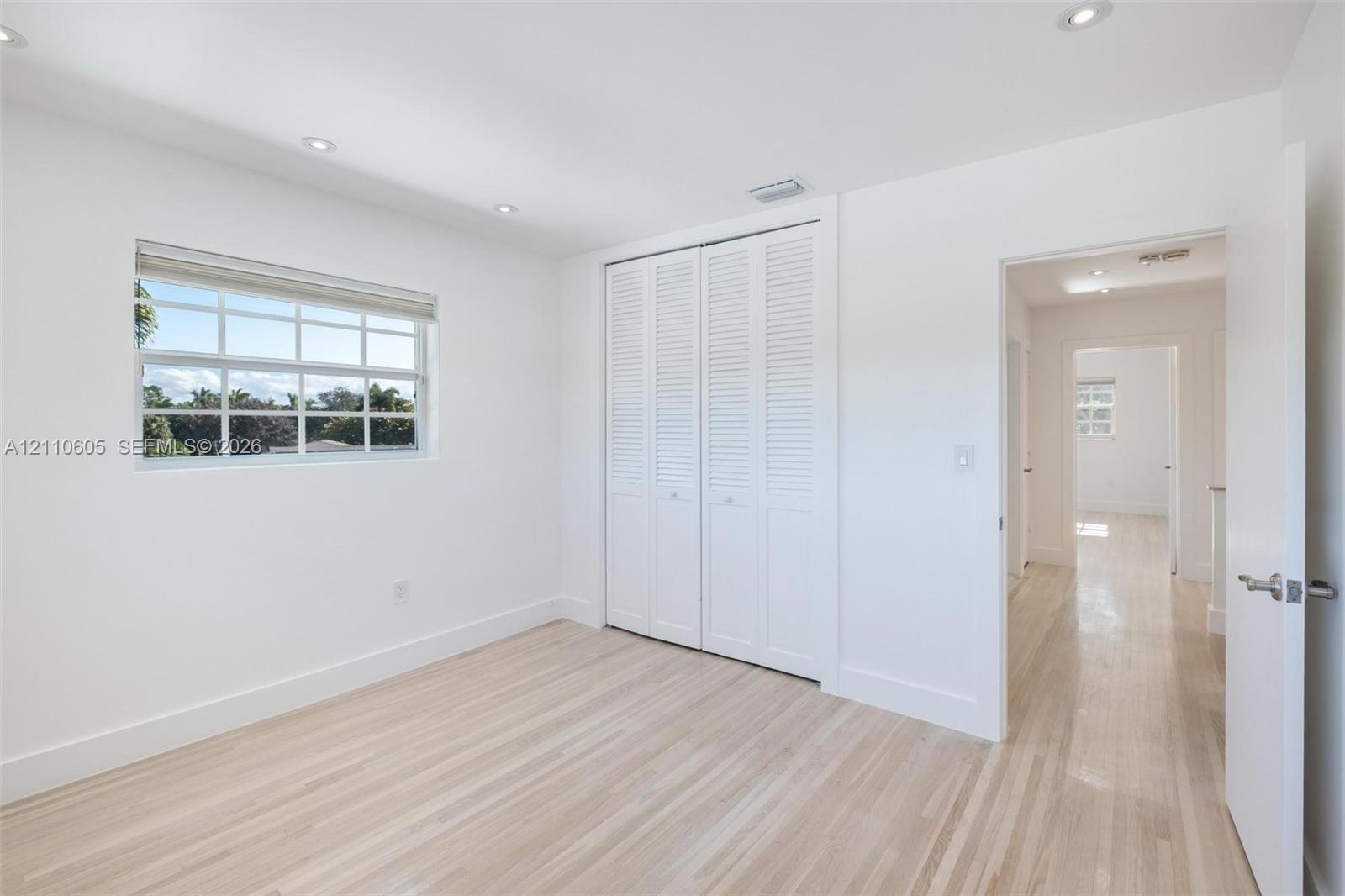 Light-filled room featuring wood-finish flooring, recessed lighting, double louvered closet doors, and multi-pane window