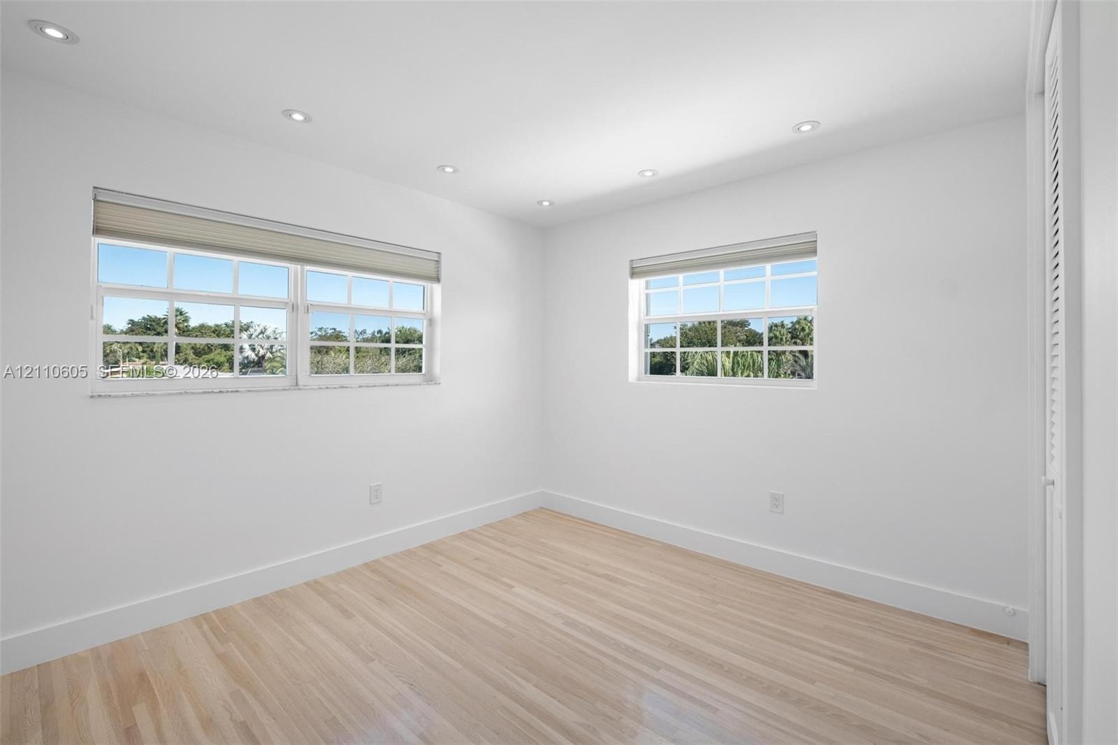 Interior space featuring wood-finish flooring, recessed lighting, multi-pane windows with fitted shades, and louvered closet doors
