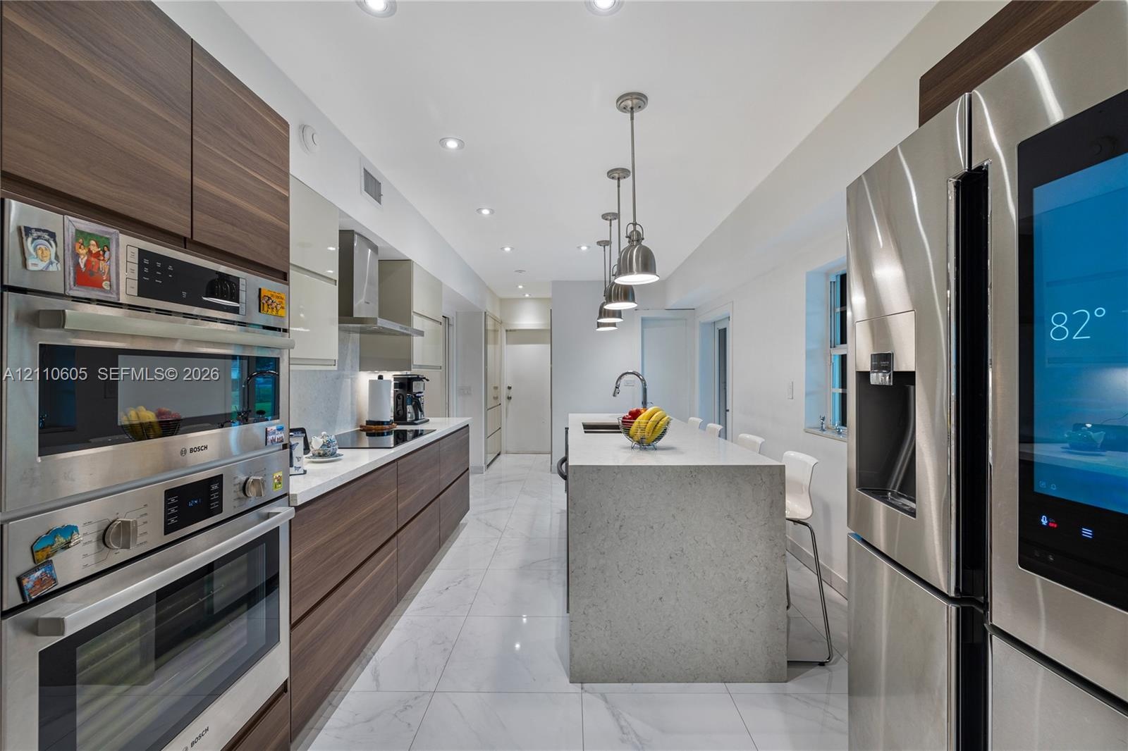 Modern kitchen featuring wood-finish cabinetry, a central island with a solid surface countertop, stainless steel appliances, large-format tile floori