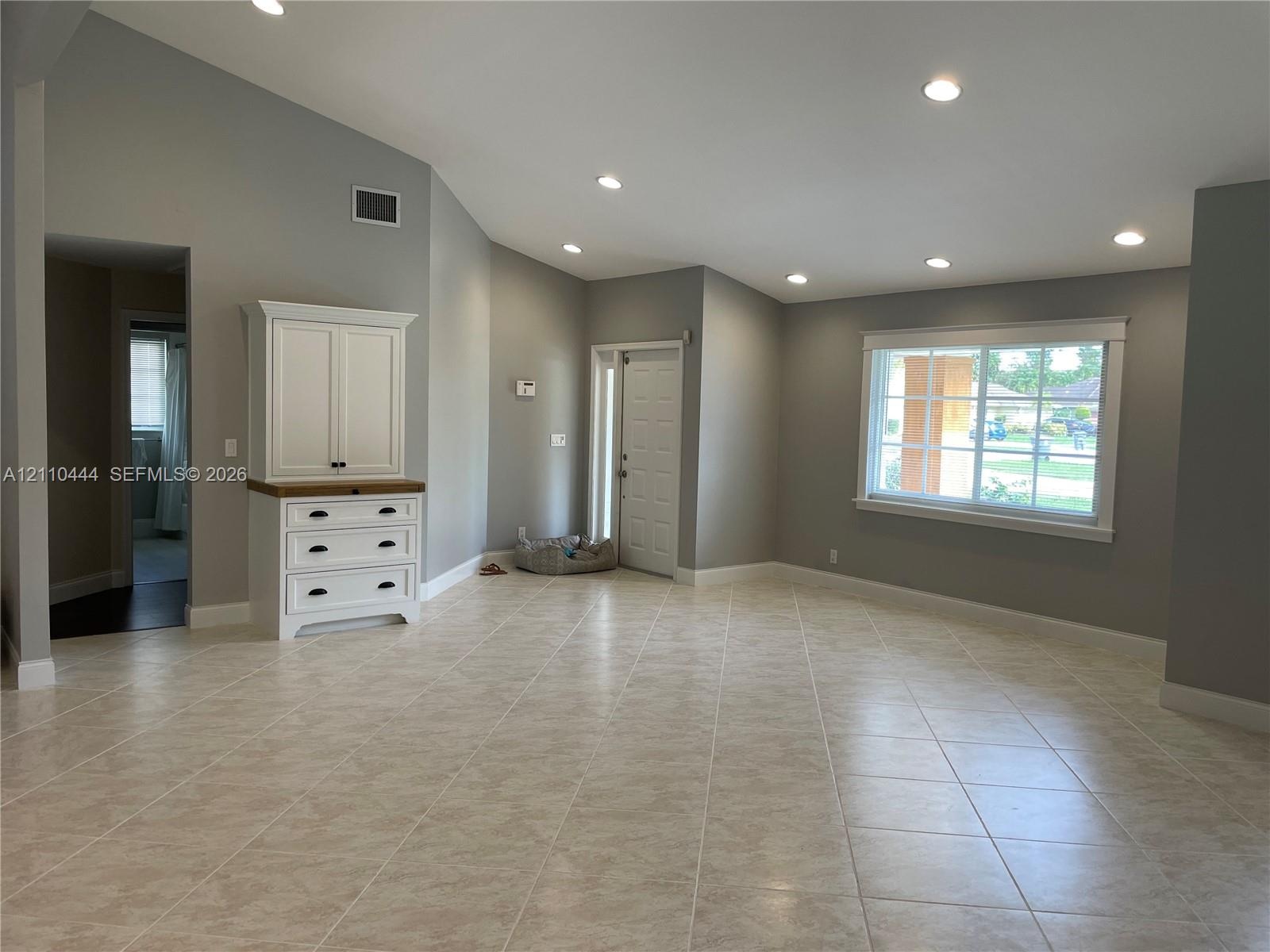 Vaulted ceilings featuring recessed lighting, large-format tile flooring, built-in cabinetry with a wood-tone surface, and a multi-pane window