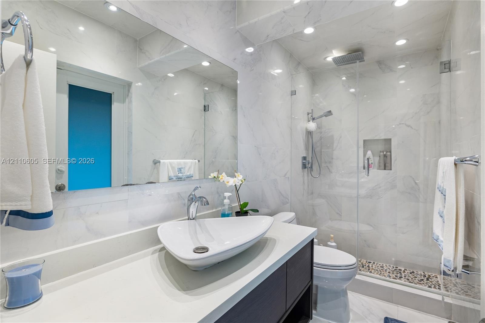 Bathroom featuring full-height stone-finish wall tile, frameless glass shower enclosure, recessed shower niche, vessel sink with chrome hardware, and 