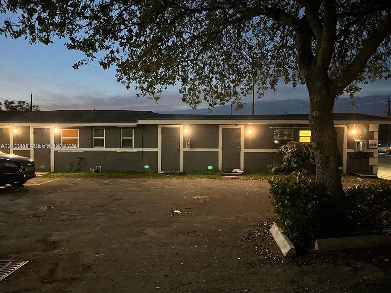 Single-story exterior featuring a dark grey finish, paved parking area, and mature canopy tree