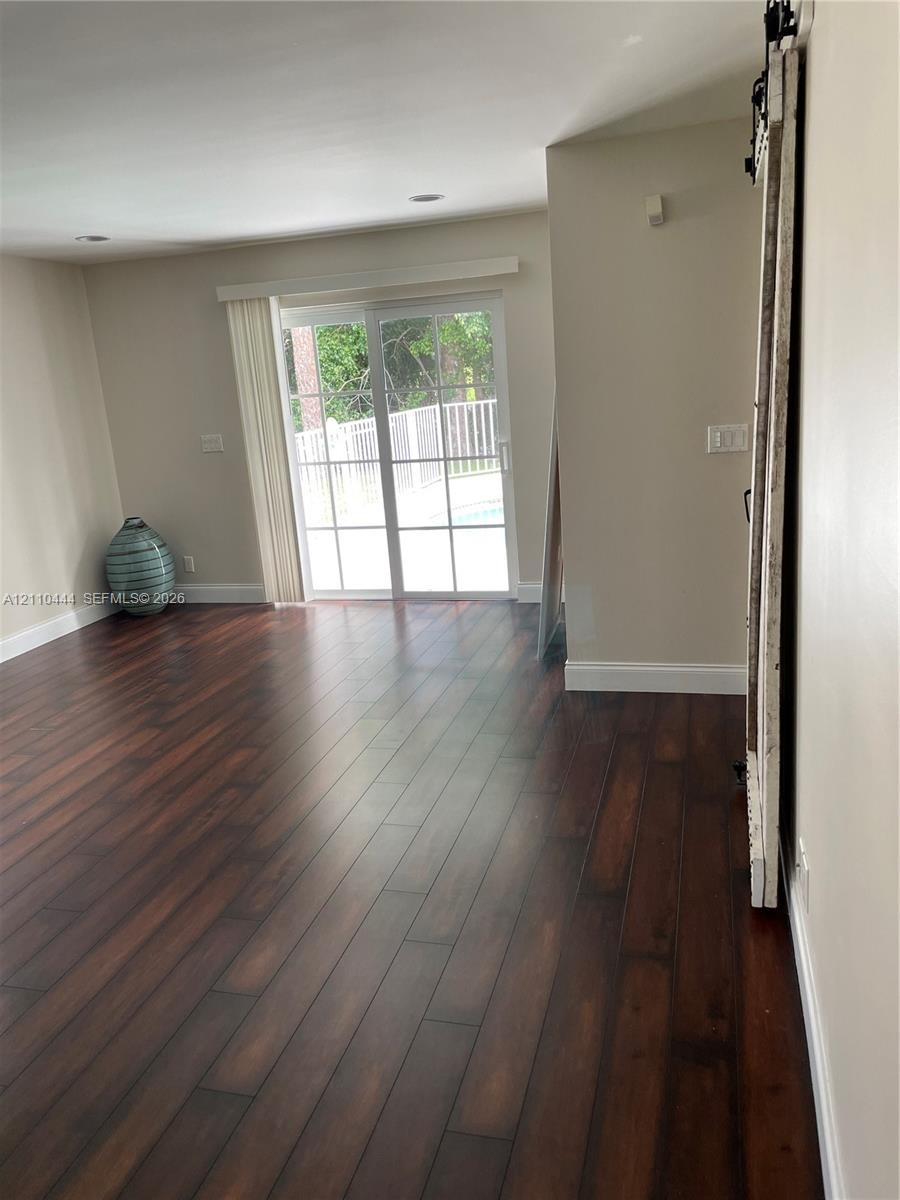 Wood-finish flooring, sliding glass patio door with muntins, recessed ceiling lighting, and a mounted rustic-style sliding barn door