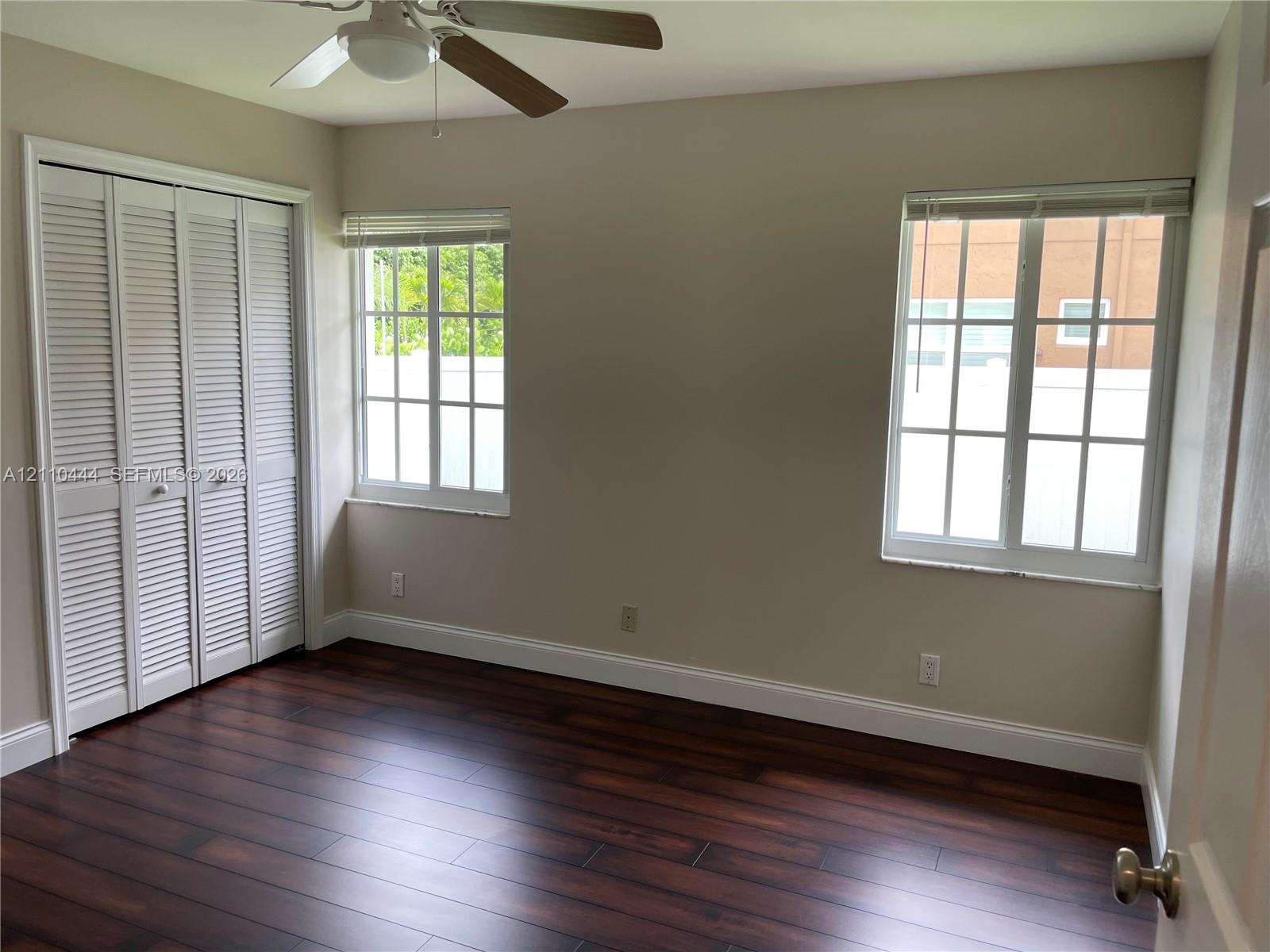 Wood-finish flooring, dual windows with divided-light panes, bi-fold closet doors, and ceiling fan with integrated lighting