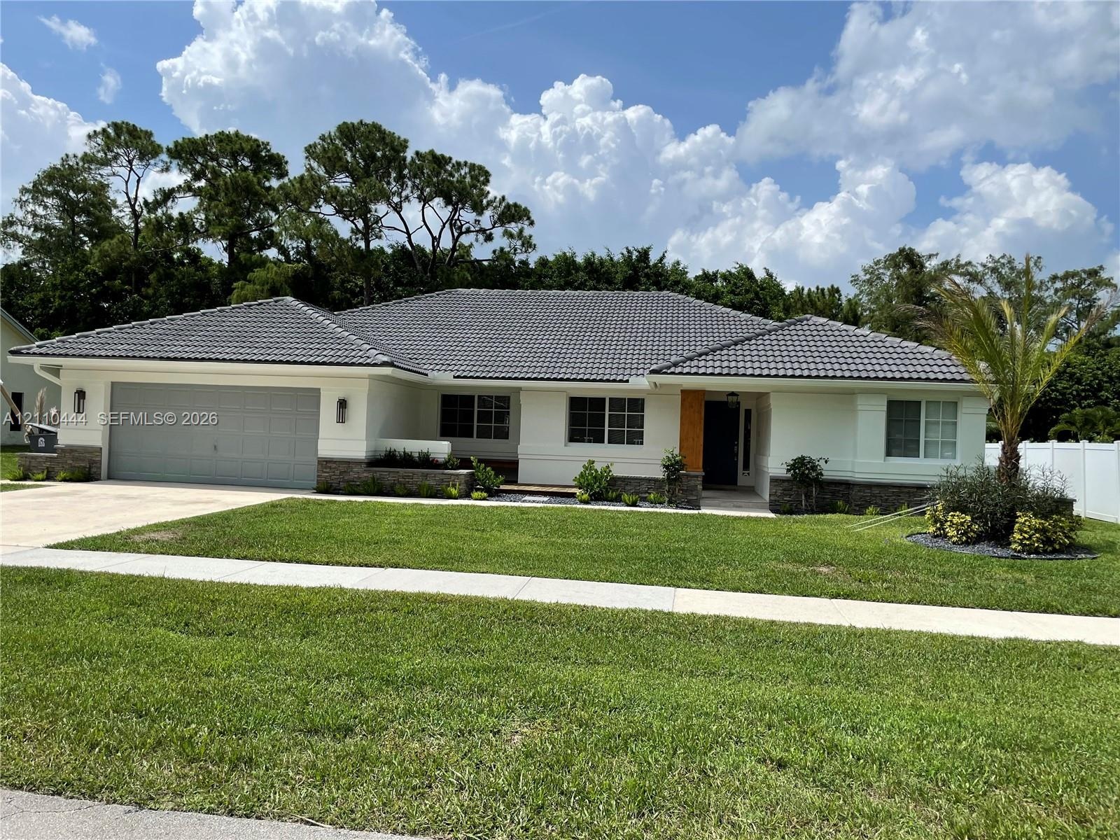 Single-story exterior featuring a gray tile roof, stone veneer accents, multi-pane windows, and a wide paved driveway