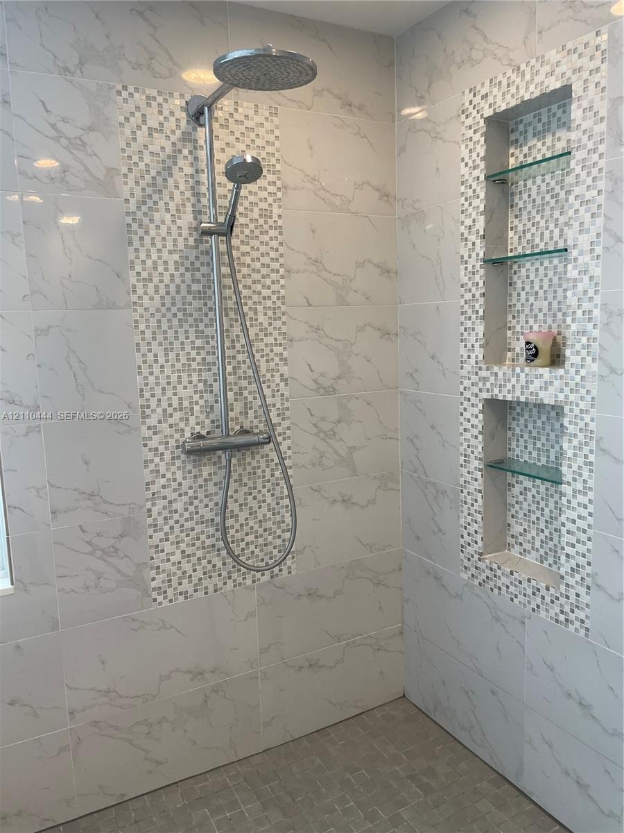 Walk-in shower featuring large-format stone-patterned wall tiles, decorative mosaic accent tiling, a rainfall showerhead with a handheld sprayer, and 