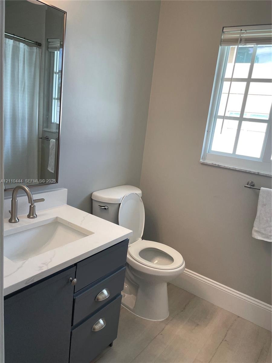 Bathroom featuring a vanity with dark cabinetry, stone-finish countertop, undermount sink, and arched-spout faucet, complemented by wood-finish floori