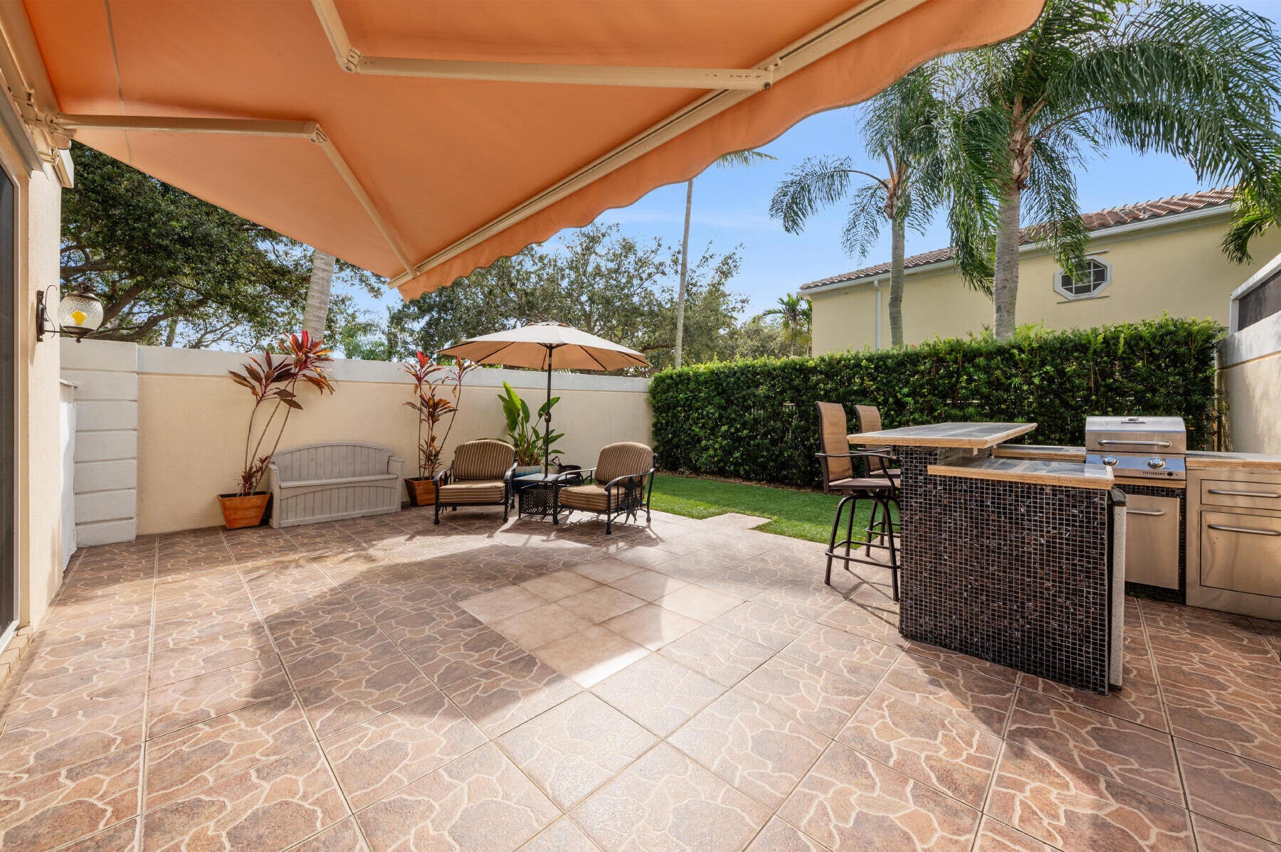 Outdoor patio featuring a retractable awning, tiled flooring, and a built-in outdoor kitchen with stainless steel appliances and mosaic tile detailing