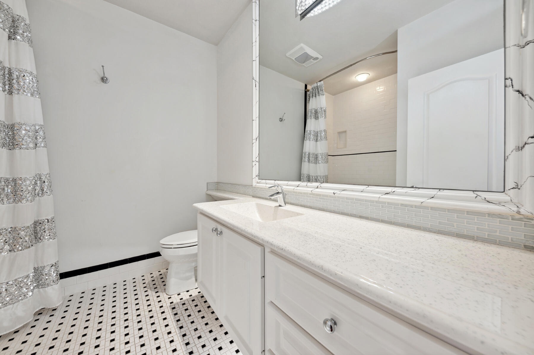Bathroom featuring a vanity with a light-toned solid surface countertop, an integrated rectangular sink, a large framed mirror, and mosaic-style floor