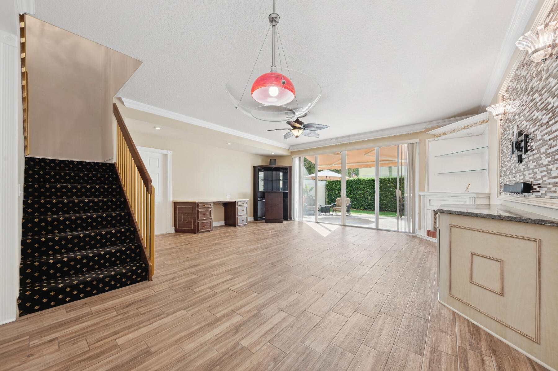 Open-concept interior featuring wood-finish flooring, a built-in stone-top wet bar, floor-to-ceiling glass sliding doors, and a decorative tile accent