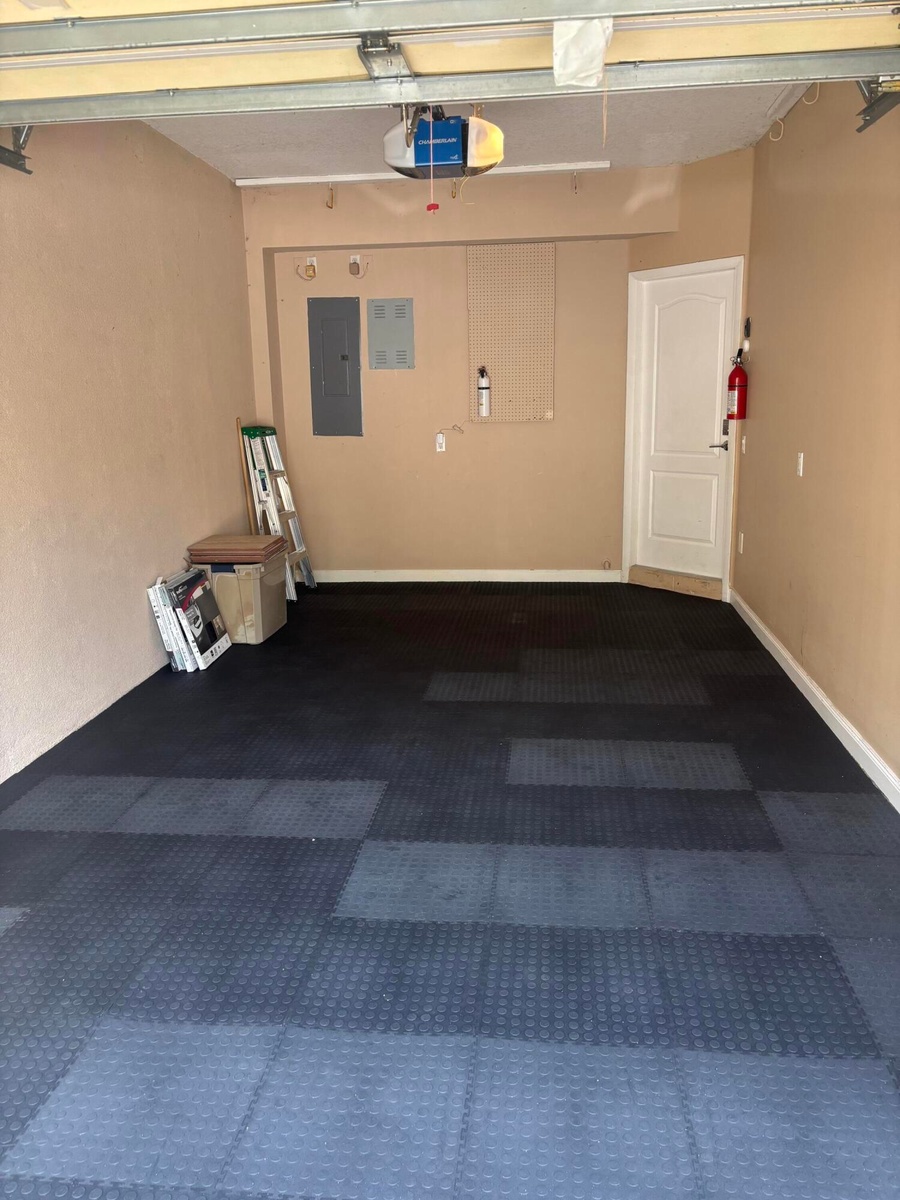 Garage interior featuring modular rubberized flooring, an automated overhead door opener, and a panel-style interior door