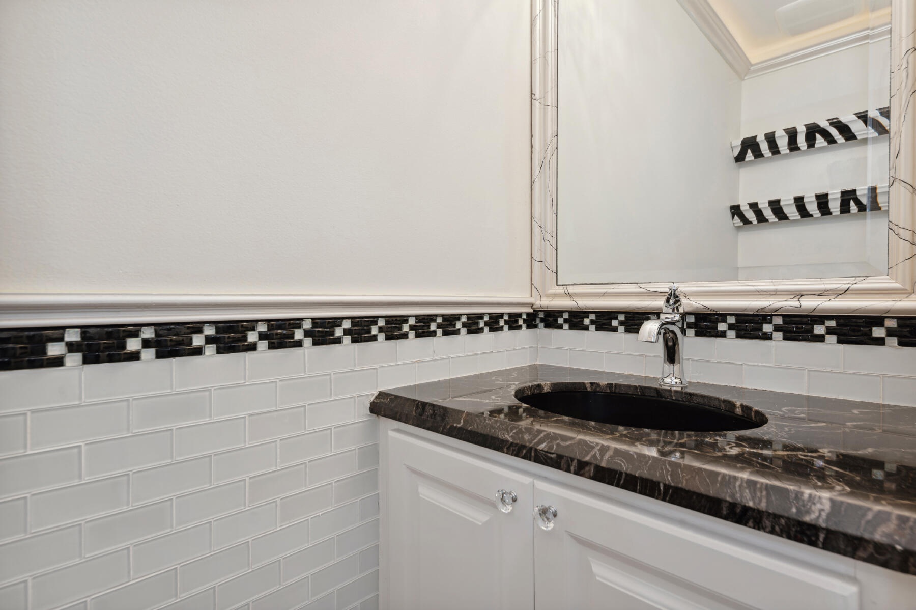Vanity featuring a dark stone countertop, undermount oval sink, polished chrome faucet, white cabinetry with crystal-style hardware, and a subway tile