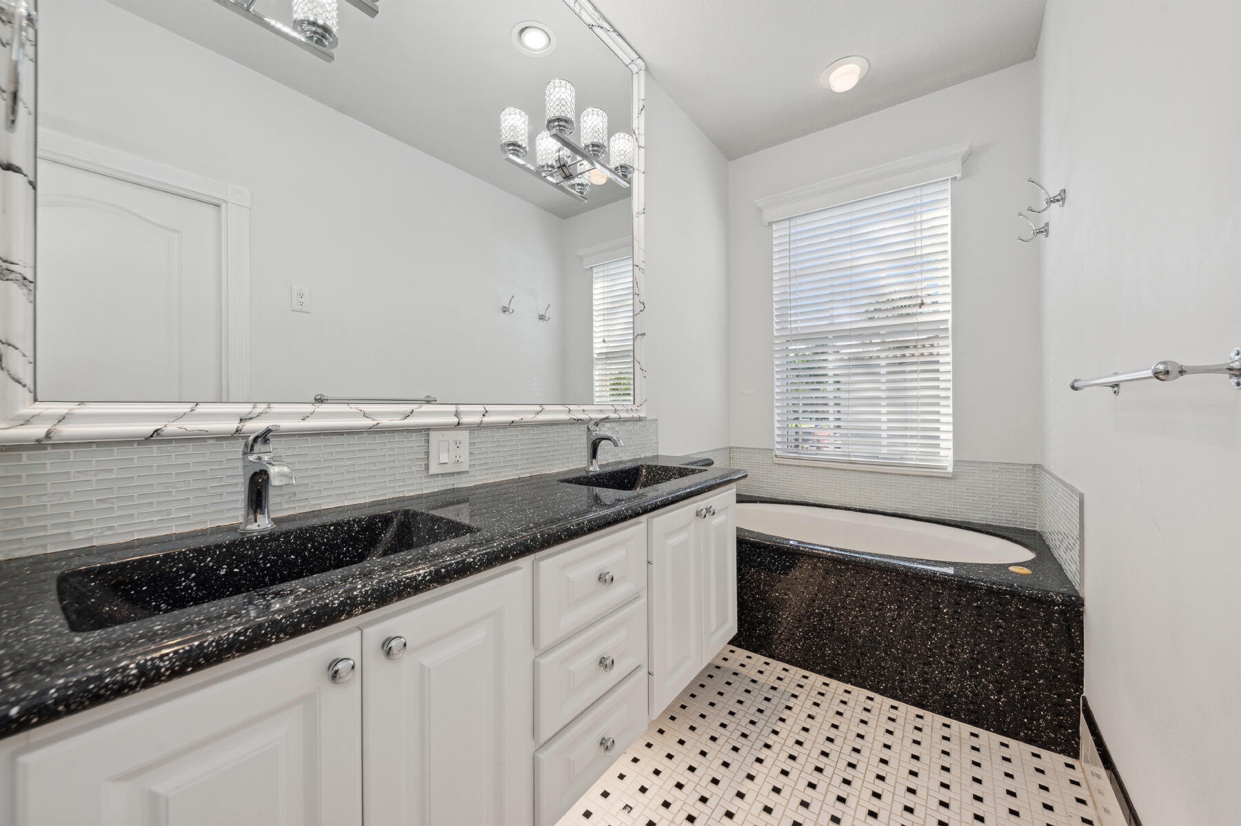 Dual-sink vanity with stone-finish countertops, undermount sinks, white cabinetry, integrated soaking tub, and decorative wall-to-wall mirror with fra