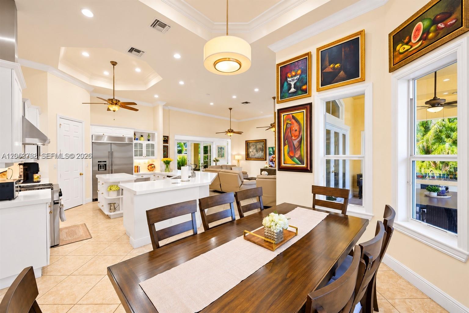 Open-concept kitchen and dining area featuring tray ceilings with crown molding, recessed lighting, tile flooring, built-in white cabinetry, and stain