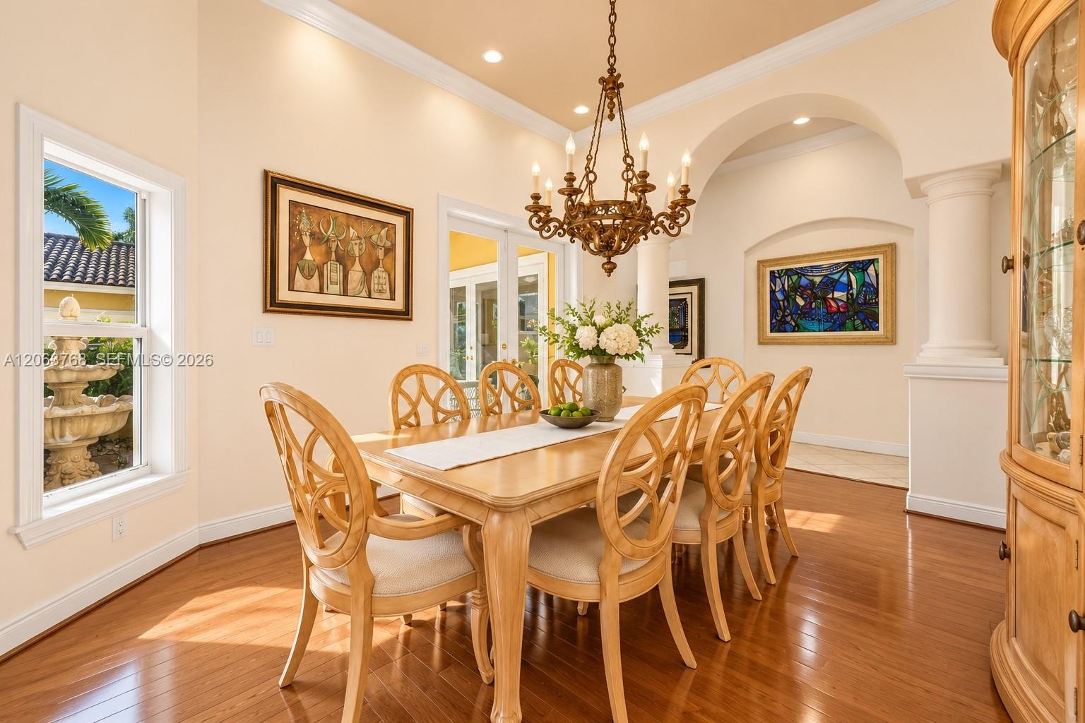 Dining area featuring wood-finish flooring, a decorative chandelier, architectural columns, a recessed archway, and crown molding