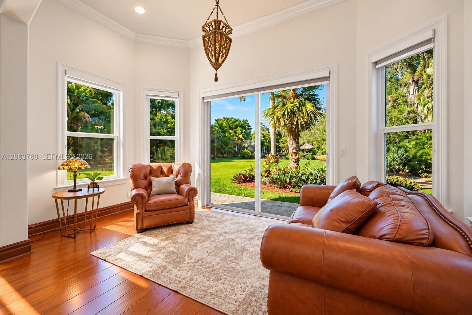 Sun-filled room featuring wood-finish flooring, crown molding, a decorative hanging pendant fixture, and expansive windows with sliding glass doors op