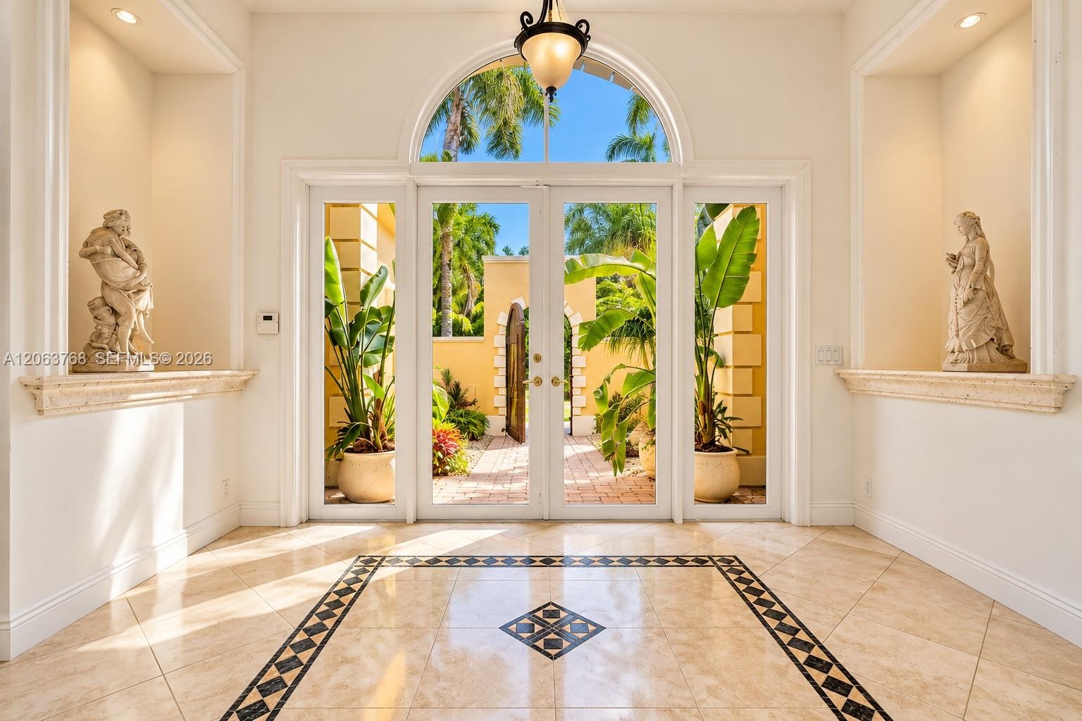 Entryway featuring double glass doors with a rounded transom window, polished stone tile flooring with a decorative geometric inlay, dual recessed wal