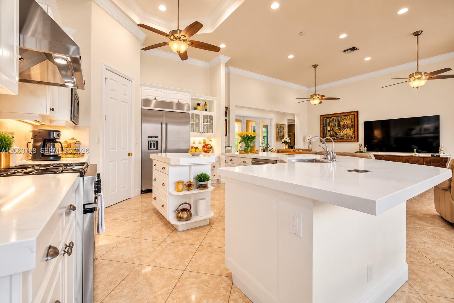 Kitchen featuring white cabinetry, solid-surface countertops, a center island with built-in shelving, stainless steel appliances, and tile flooring