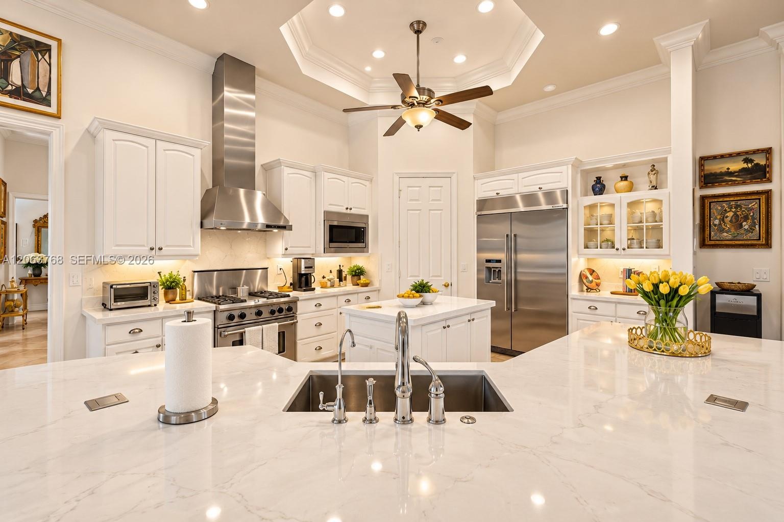 Gourmet kitchen featuring a large central island with a quartz countertop, stainless steel appliances, white cabinetry with glass-front display sectio