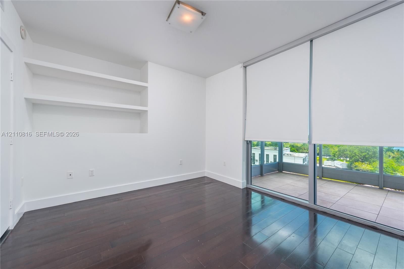 Interior space featuring dark wood-finish flooring, built-in recessed shelving, floor-to-ceiling glass sliding doors, and an attached balcony with til
