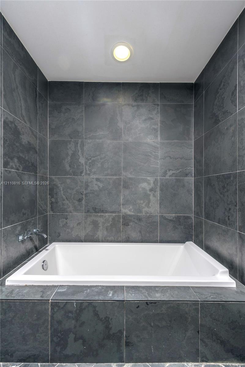 Built-in soaking tub featuring a white acrylic finish, surrounded by charcoal-toned stone tile surround and matching full-height tiled wall accents wi