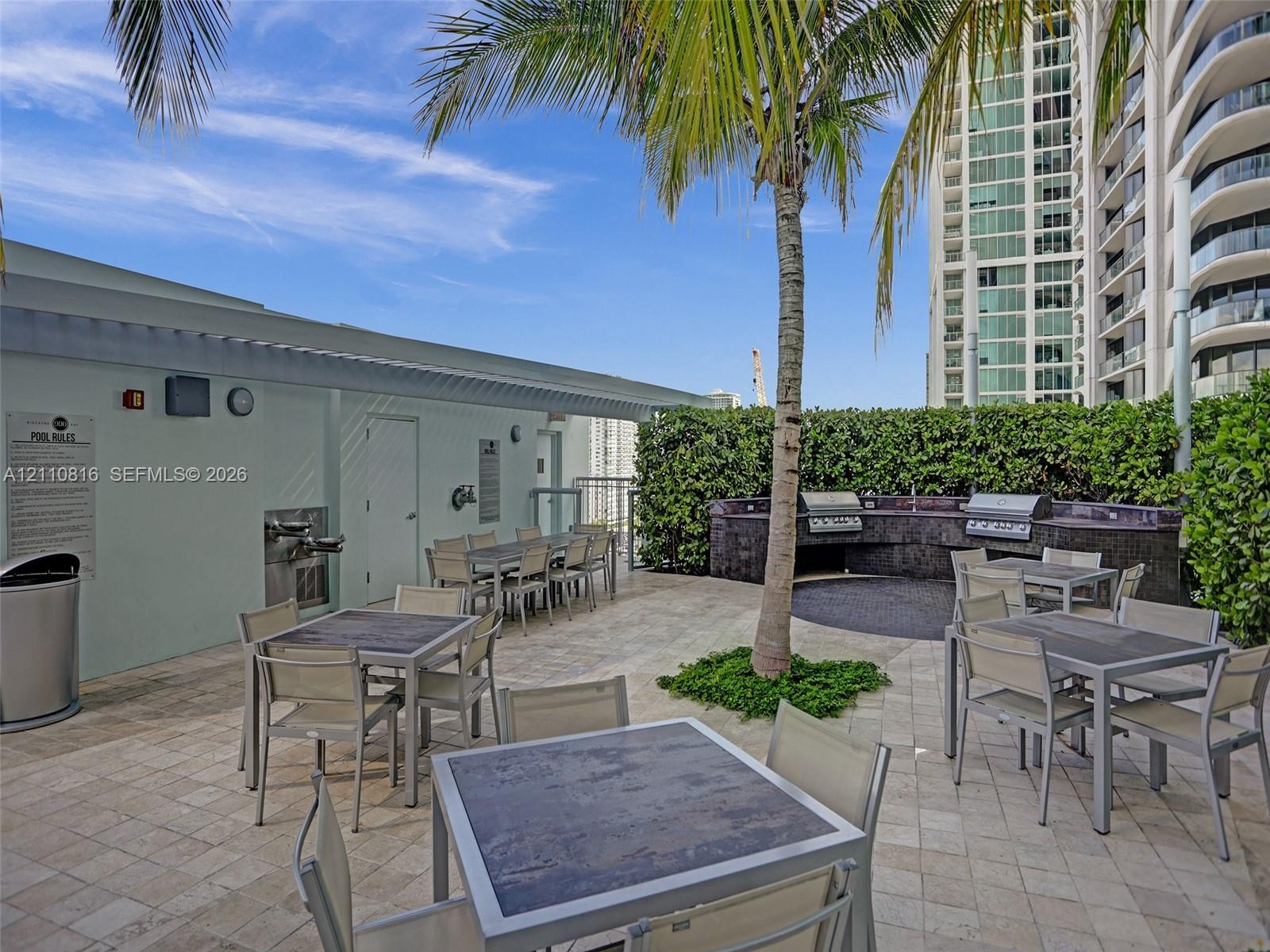 Outdoor terrace featuring stone-tile flooring, a built-in stone-finished kitchen station with integrated stainless steel grills, a manicured hedge per
