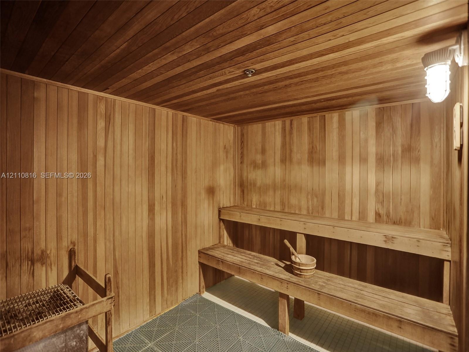 Sauna interior featuring natural wood-paneled walls and ceiling, multi-level tiered wooden benches, an integrated stone heater, and industrial-style w